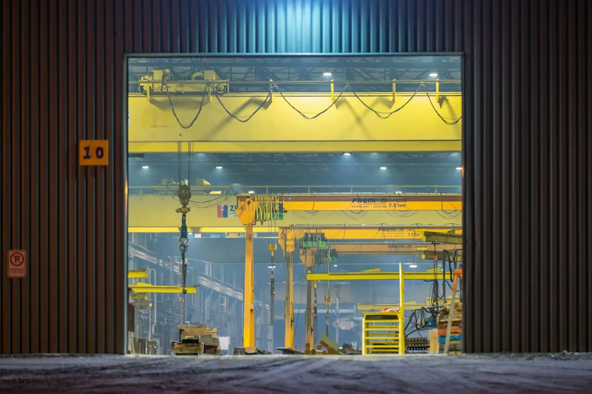 Open industrial door with the lit shop floor and crane behind it